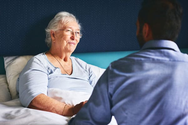 caregiver talking with patient in bed at home | TLC Your Way Hospice Care